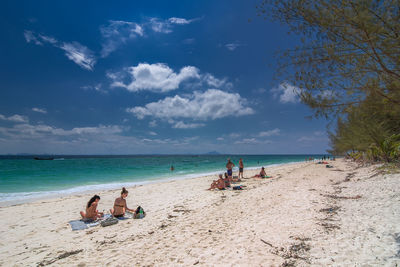 People relaxing on beach against sky