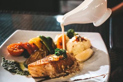 Close-up of cream being poured on meat in plate