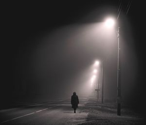 Rear view of person walking on illuminated street at night