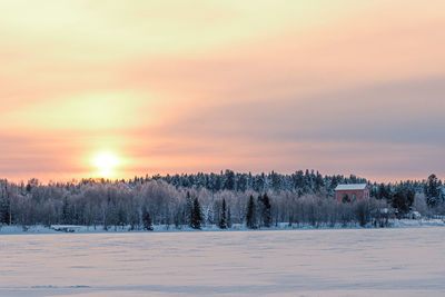 Snow covered land against sky during sunset