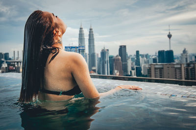 Rear view of woman in swimming pool against buildings in city