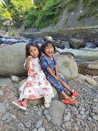 Portrait of smiling friends sitting on rock