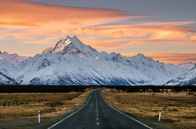 Road by snowcapped mountains against sky during sunset