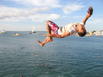 Man doing back flip over sea against sky