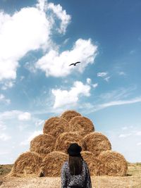 Rear view of woman standing in front of haystack against cloudy sky