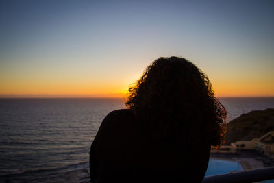 Rear view of woman against sea during sunset