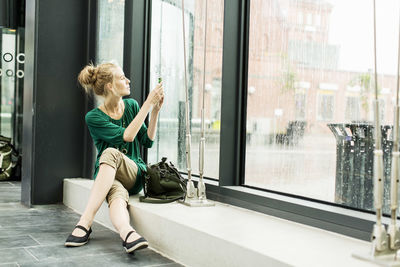 Woman photographing through glass while sitting on sill