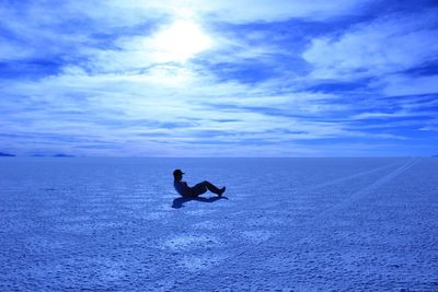 Side view of young man exercising on landscape against cloudy sky during sunny day