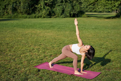 Full length of young woman exercising on field