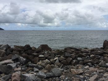 View of rocky beach against cloudy sky