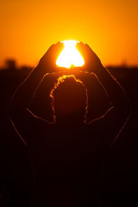 Optical illusion of silhouette man holding sun against orange sky