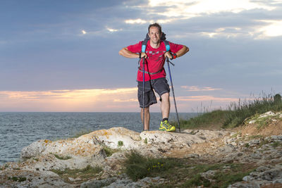 Portrait of smiling mature man standing on cliff against sea at sunset