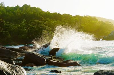 Water splashing on rocks by sea against sky