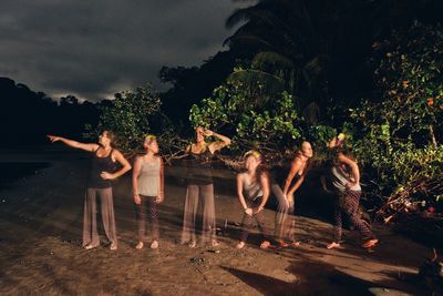 Multiple image of friends enjoying at beach against trees during night