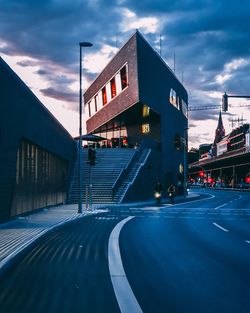 Road by illuminated city against sky at dusk