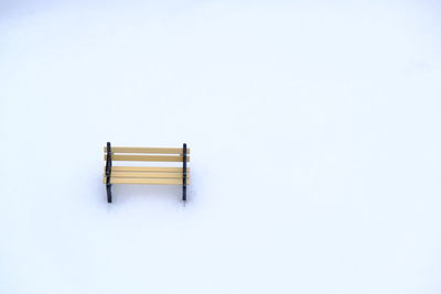 Bench on snow covered field against clear sky