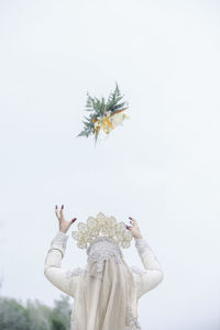 Rear view of bride throwing bouquet while standing against clear sky