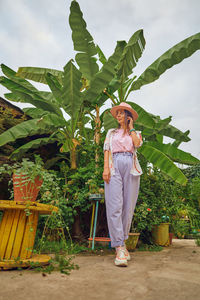 Full length portrait of smiling woman standing against plants