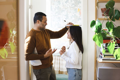 Smiling father measuring height of excited daughter at doorway of home