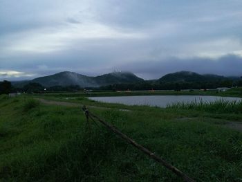 Scenic view of field by lake against sky