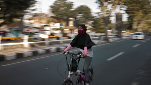 Rear view of woman riding bicycle on road in city