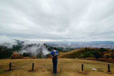 Woman standing on field against cloudy sky