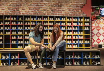 Man helping young woman tying shoes at bowling alley