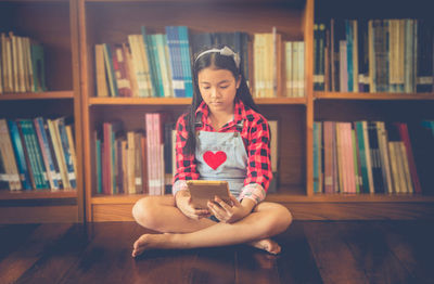 Young woman using phone while sitting on book