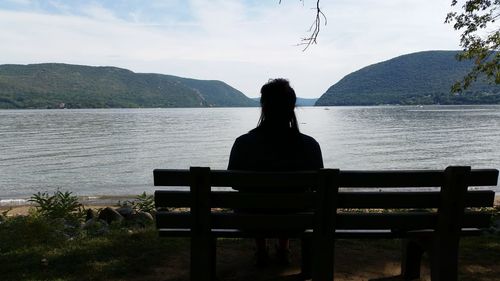 Rear view of man sitting on bench at lakeshore