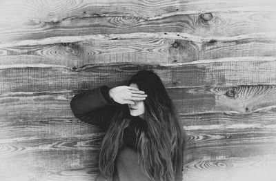 Young woman covering eyes against wooden wall