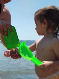 Full length of shirtless boy holding water while standing on beach