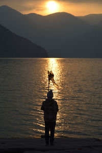 Silhouette of man fishing in sea against sunset sky