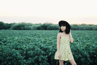 Young woman standing on field against sky