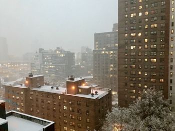 Illuminated buildings in city against sky during winter