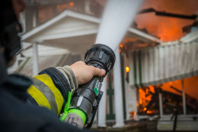 Close-up of a firefighter spraying burning house with hose