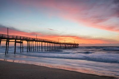 Wooden jetty on beach against cloudy sky