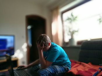 Frustrated teenage boy using laptop with head in hand at home