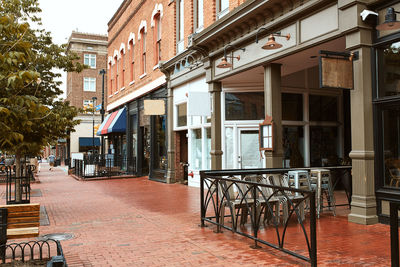 Empty chairs and tables on street by buildings in city