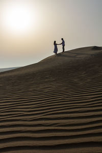 People on sand dune at beach against clear sky