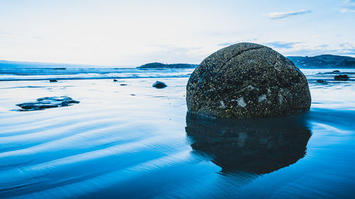 Reflection of rocks on sea shore against sky
