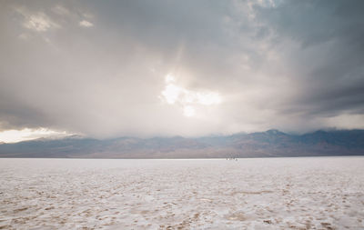 Scenic view of snow covered arid landscape against cloudy sky at death valley national park
