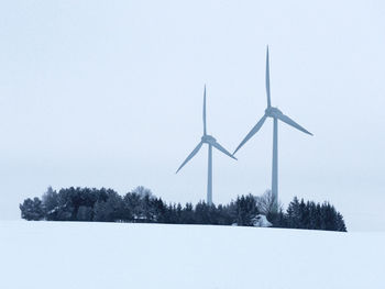 Wind turbines on field against sky during winter