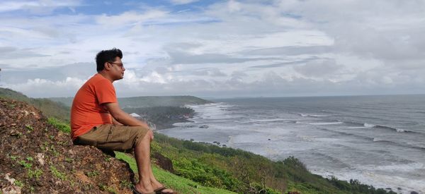 Side view of young man looking at sea against sky