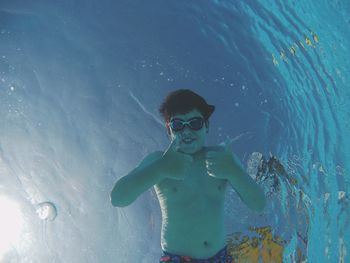 Directly below portrait of shirtless boy gesturing thumbs up in swimming pool