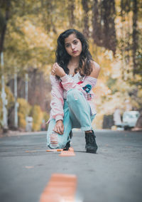 Portrait of young woman kneeling on road against trees