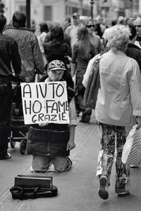 Portrait of beggar holding banner with people walking on street