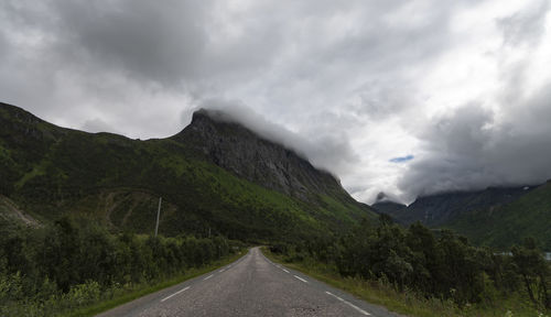 Country road leading towards mountains against sky