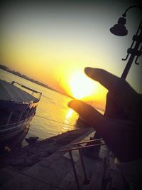 Close-up of hand holding boat against sea during sunset