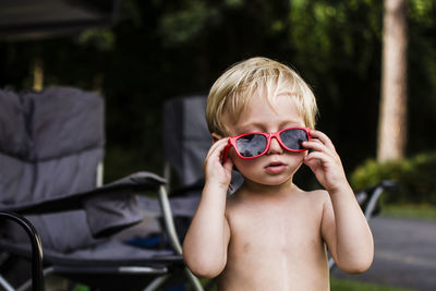 Cute shirtless boy wearing sunglasses while standing in backyard