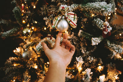 Cropped hand of woman touching illuminated christmas tree